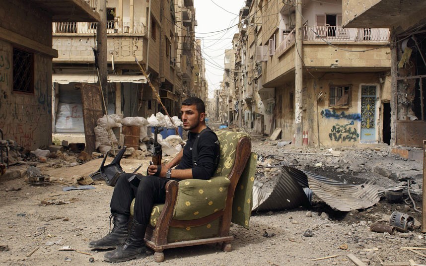 فرد من اعضاء الجيش السوري الحر يجلس على أريكة مع بندقيته بين أنقاض دير الزور